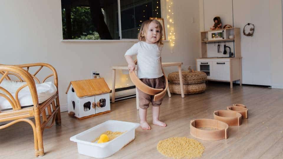 Une petite fille joue avec des jeux Montessori de découverte en toute autonomie, dans une pièce adaptée et bien rangée.