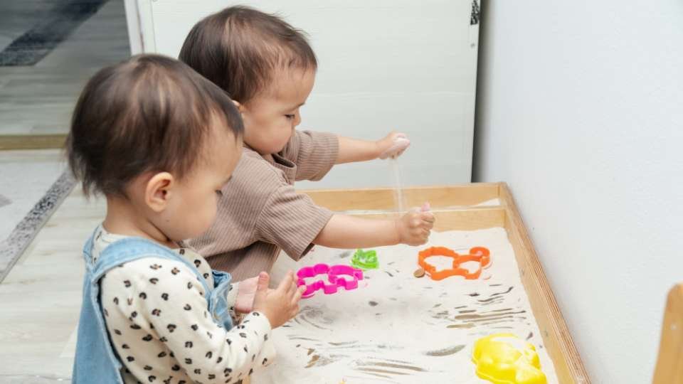 Les enfants, encouragés à être autonomes par le guide Montessori, participent à des jeux de formes dans un bac à sable qui entraine leur coordination et leur conscience de l'environnement