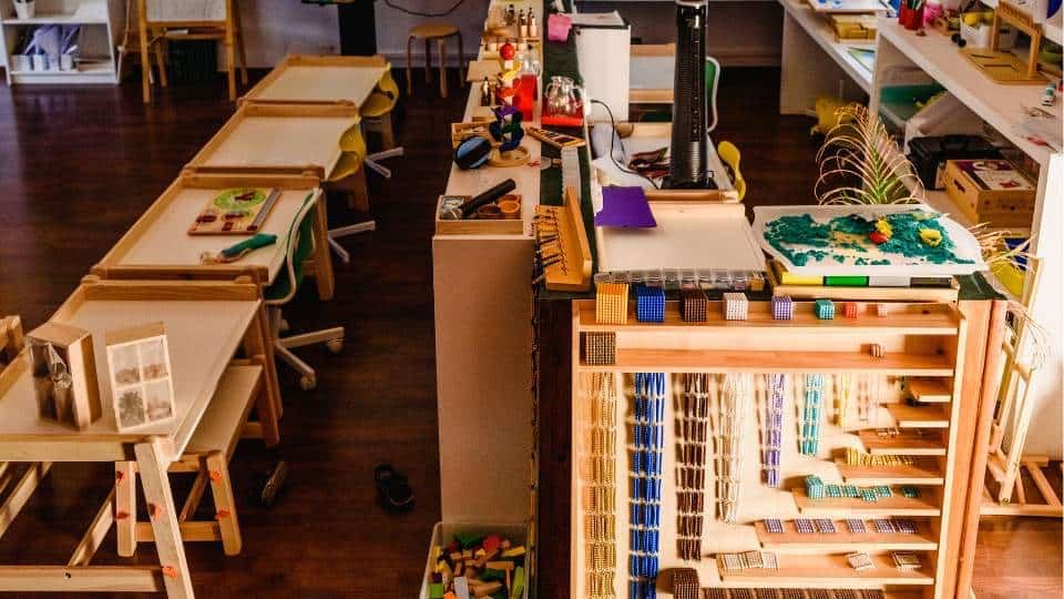 Une salle de classe Montessori pour enfants avec tables et chaises en bois, organisées et bien rangées.