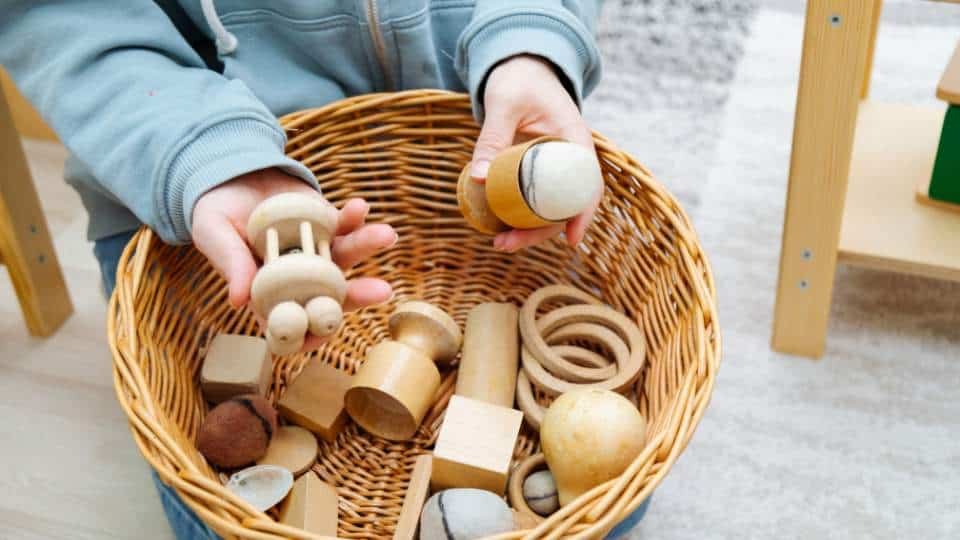 Un enfant joue avec des jouets en bois dans un panier, ce qui entraîne naturellement sa dextérité