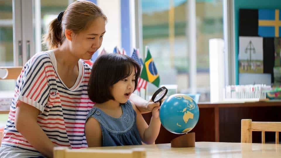 Une enseignante Montessori accompagne son élève pour regarder un globe terrestre dans la salle de classe.