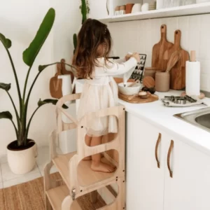 Un jeu Montessori mettant en scène une petite fille utilisant un escabeau en bois dans une cuisine.