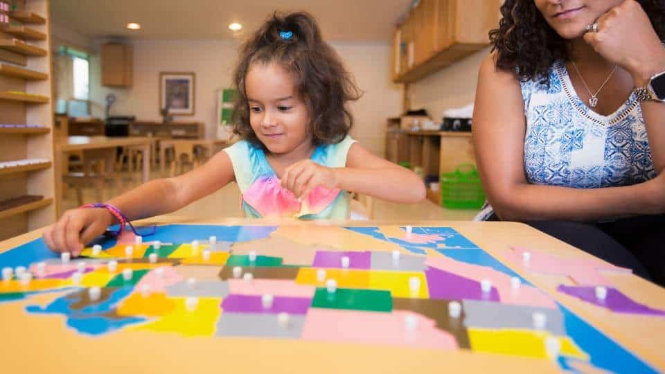 Une enfant joue avec une carte Montessori dans le salon, sous la supervision du guide.